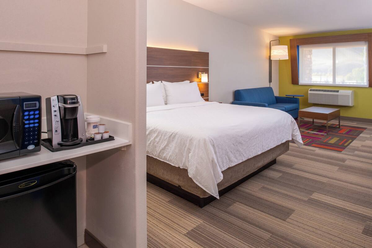 A hotel room with a bed, a desk with a coffee maker, a microwave, and a small table.