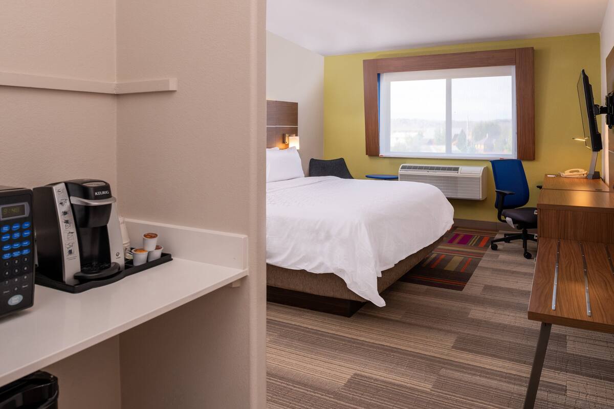 A hotel room with a bed, a desk with a computer, a coffee maker, and a window with a view.