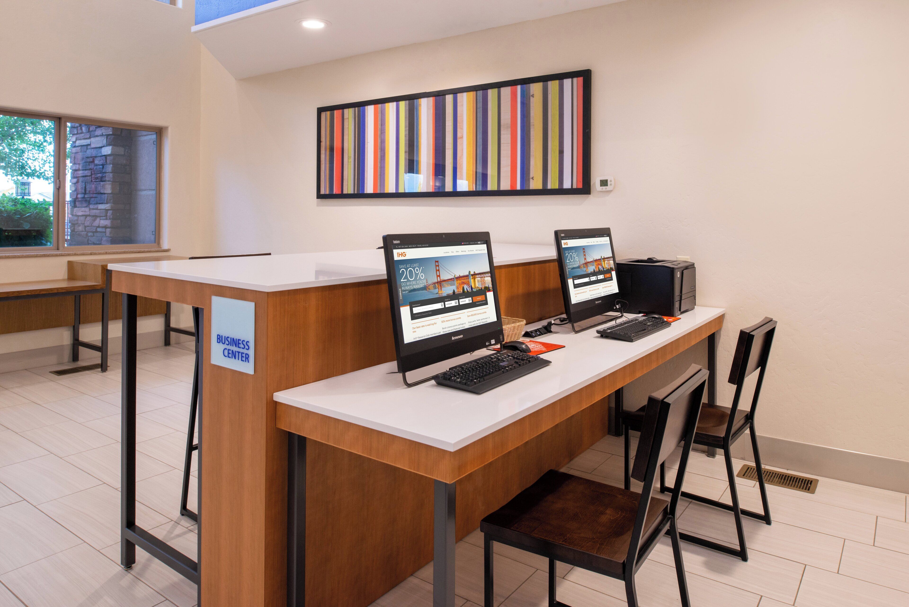 A business center with two computers, a wooden desk, and a sign indicating its location.
