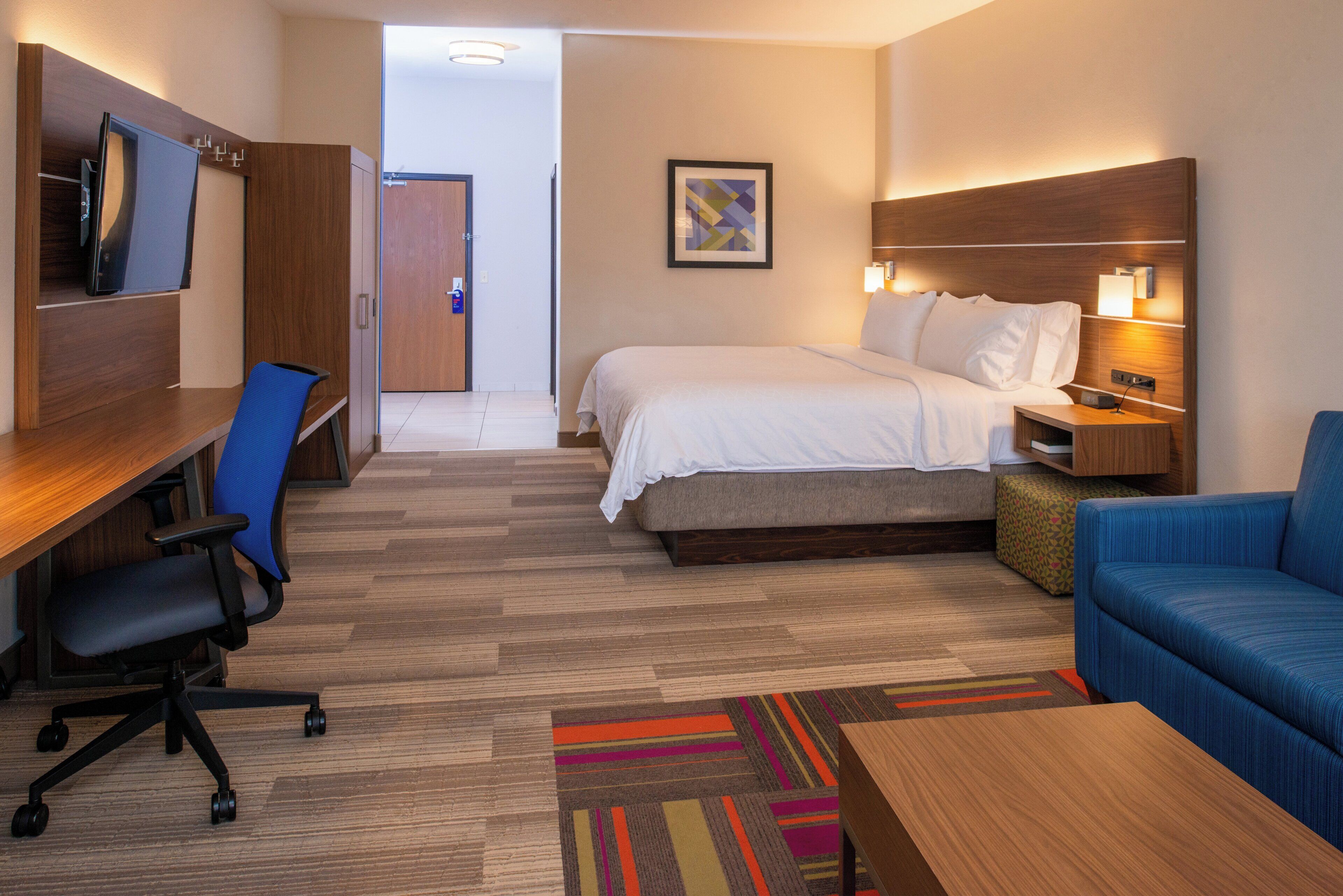 A hotel room with a bed, desk, chair, and a sofa.