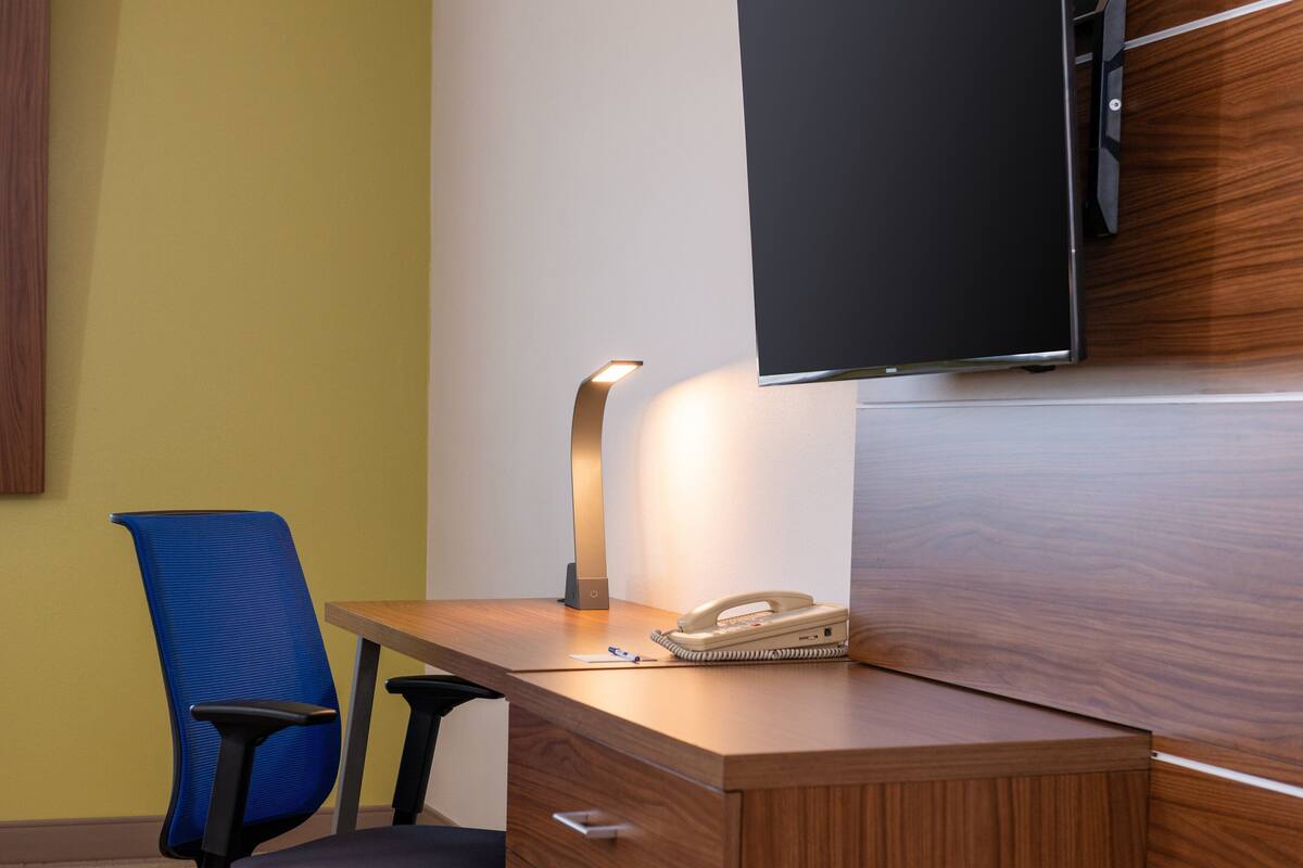 A wooden desk with a telephone, a lamp, and a blue office chair.