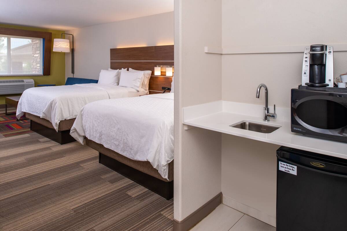 A hotel room with two beds, a kitchenette with a coffee maker, and a window with a view.