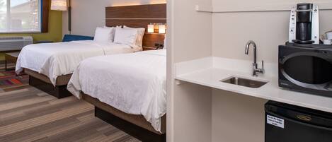 Une chambre d’hôtel avec deux lits, une kitchenette équipée d’une machine à café et une fenêtre donnant sur un paysage agréable.