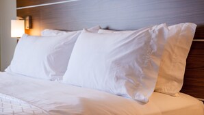 A neatly made bed with white linens and pillows, a wooden headboard, and a wall-mounted lamp. - Holiday Inn Express & Suites Gunnison by IHG (Gunnison)