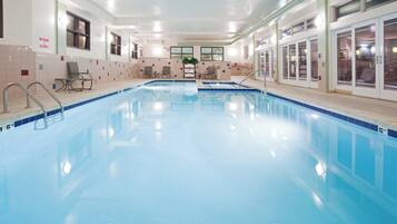 Una piscina interior cristalina con borde de azulejos, un banco y un cartel que indica que no se permite el salto.