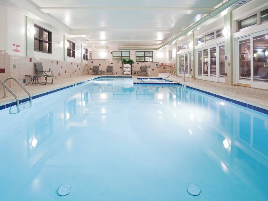Una piscina interior cristalina con borde de azulejos, un banco y un cartel que indica que no se permite el salto.