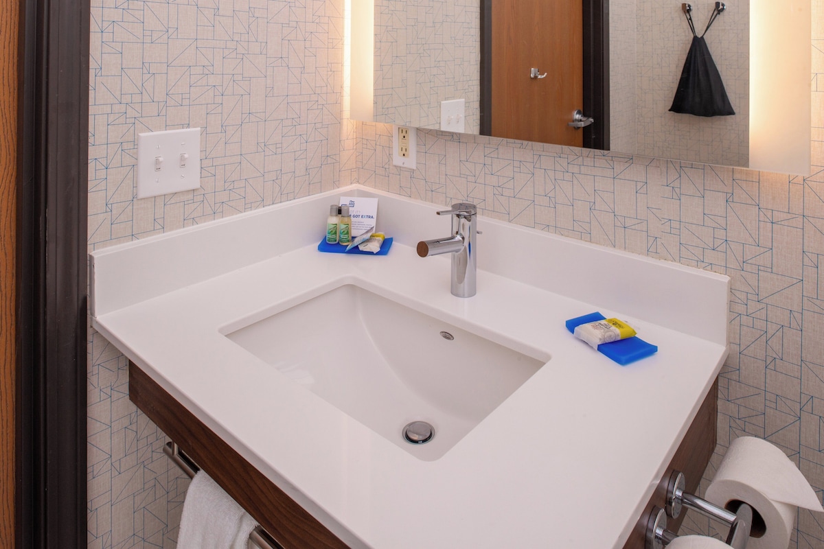 A bathroom with a white sink, a mirror, a towel rack, and a toilet paper holder.