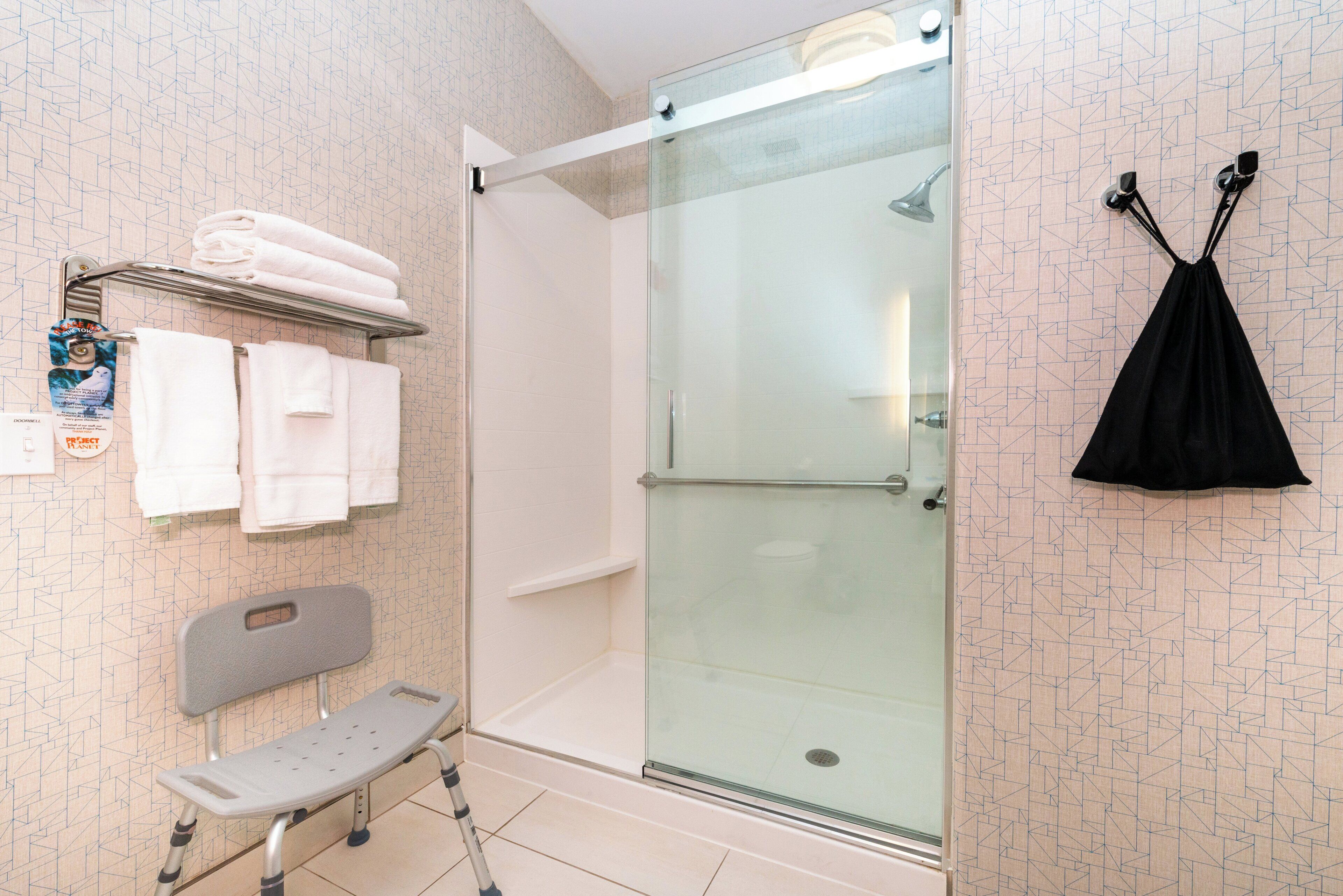 A shower with a glass door, a bench, and a towel rack with folded towels.