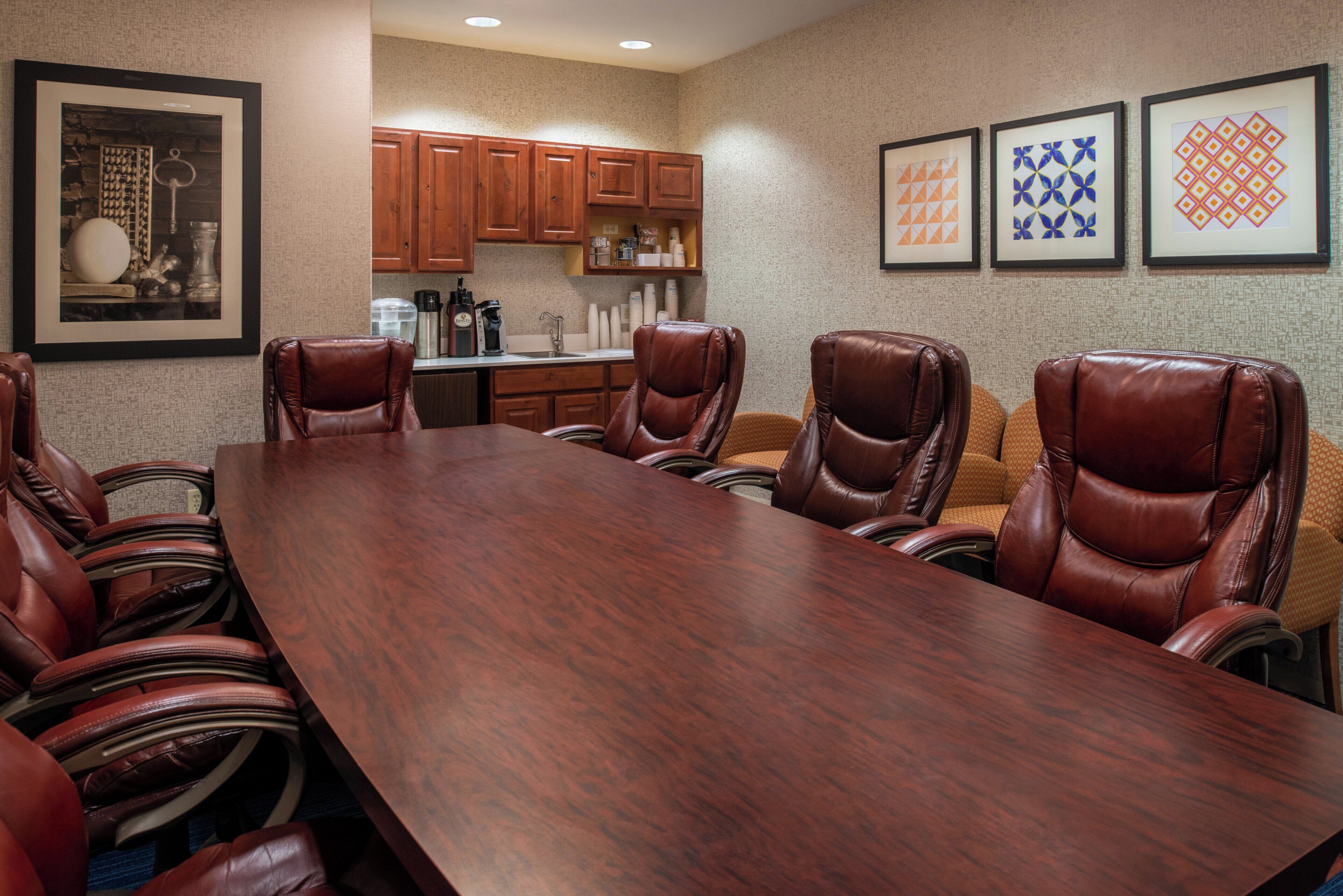 A conference room with a long wooden table and leather chairs, a kitchen area with wooden cabinets, and framed artwork on the walls.