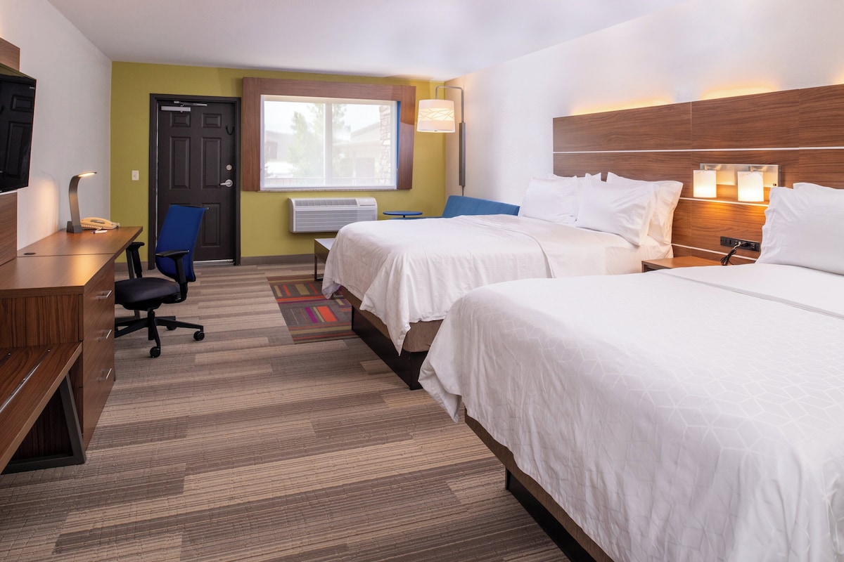 A hotel room with two beds, a desk, a chair, a TV, and a window.