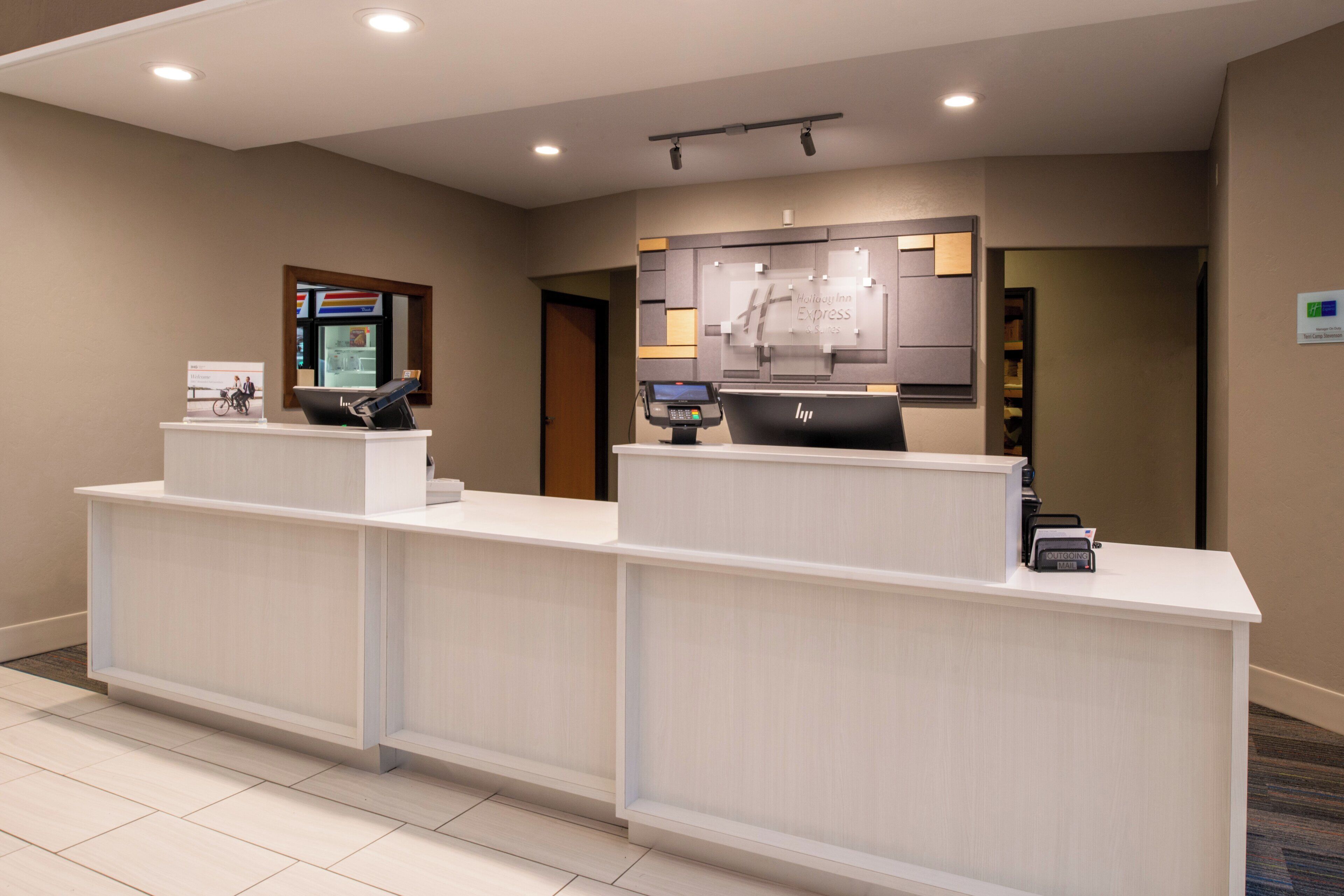 A hotel reception desk with a digital kiosk, a Holiday Inn Express sign, and a nameplate for the manager.
