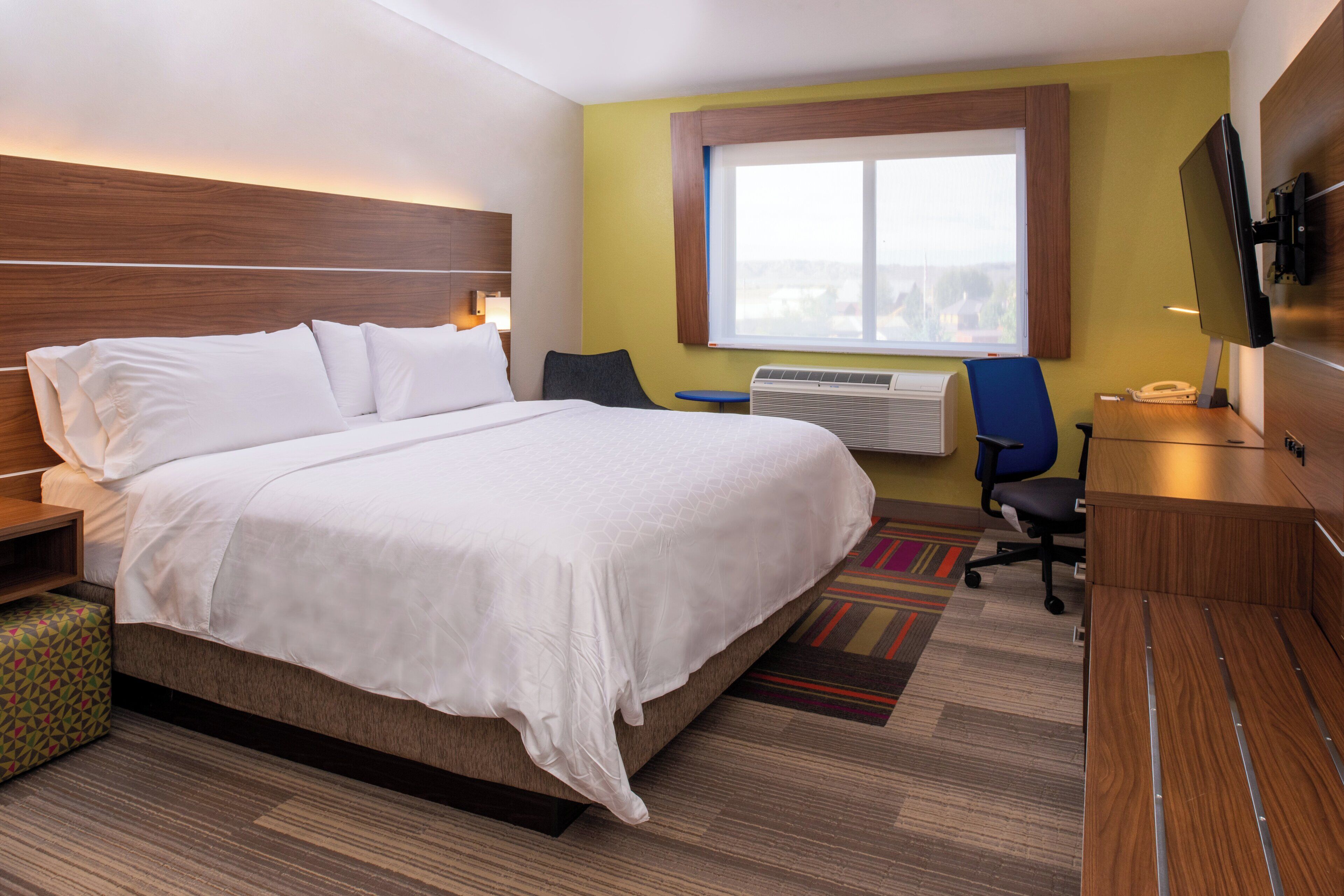 A hotel room with a large bed, a desk with a chair, a television, and a window.