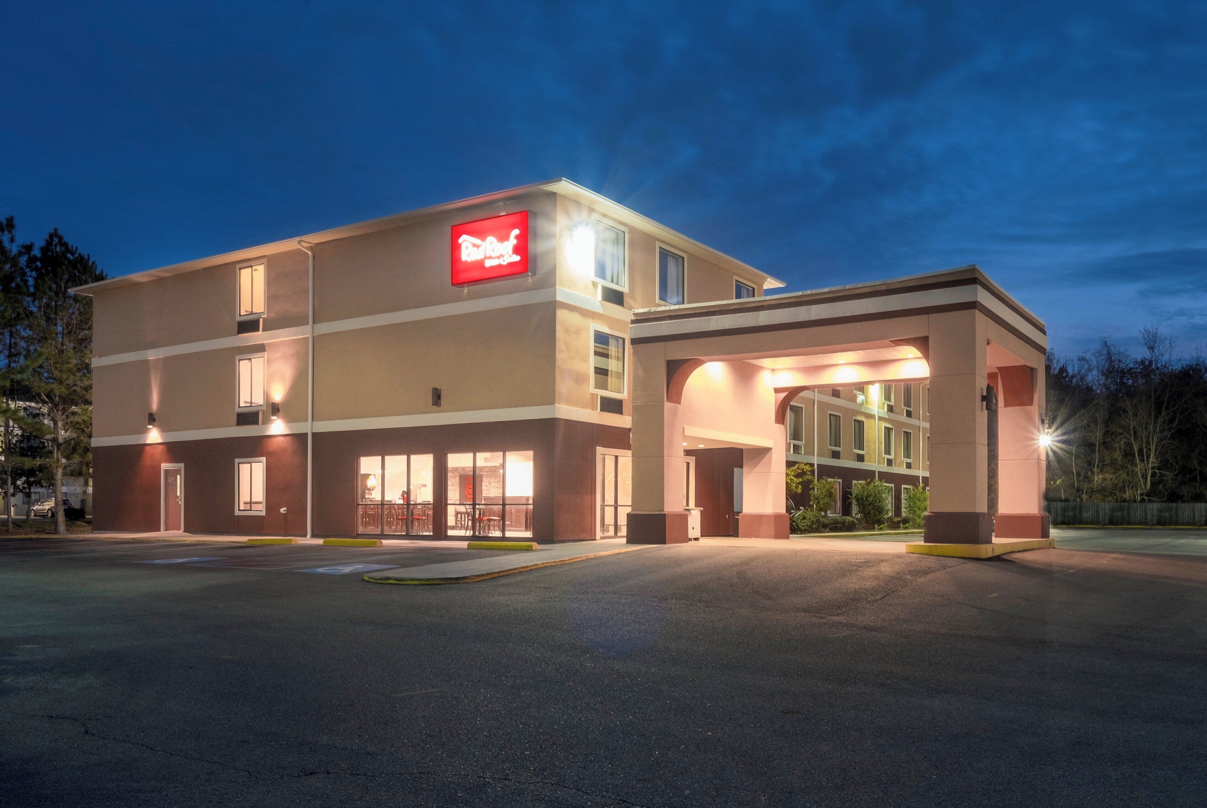 Un hôtel à plusieurs étages, reconnaissable à son grand panneau rouge, son entrée abritée et son parking.