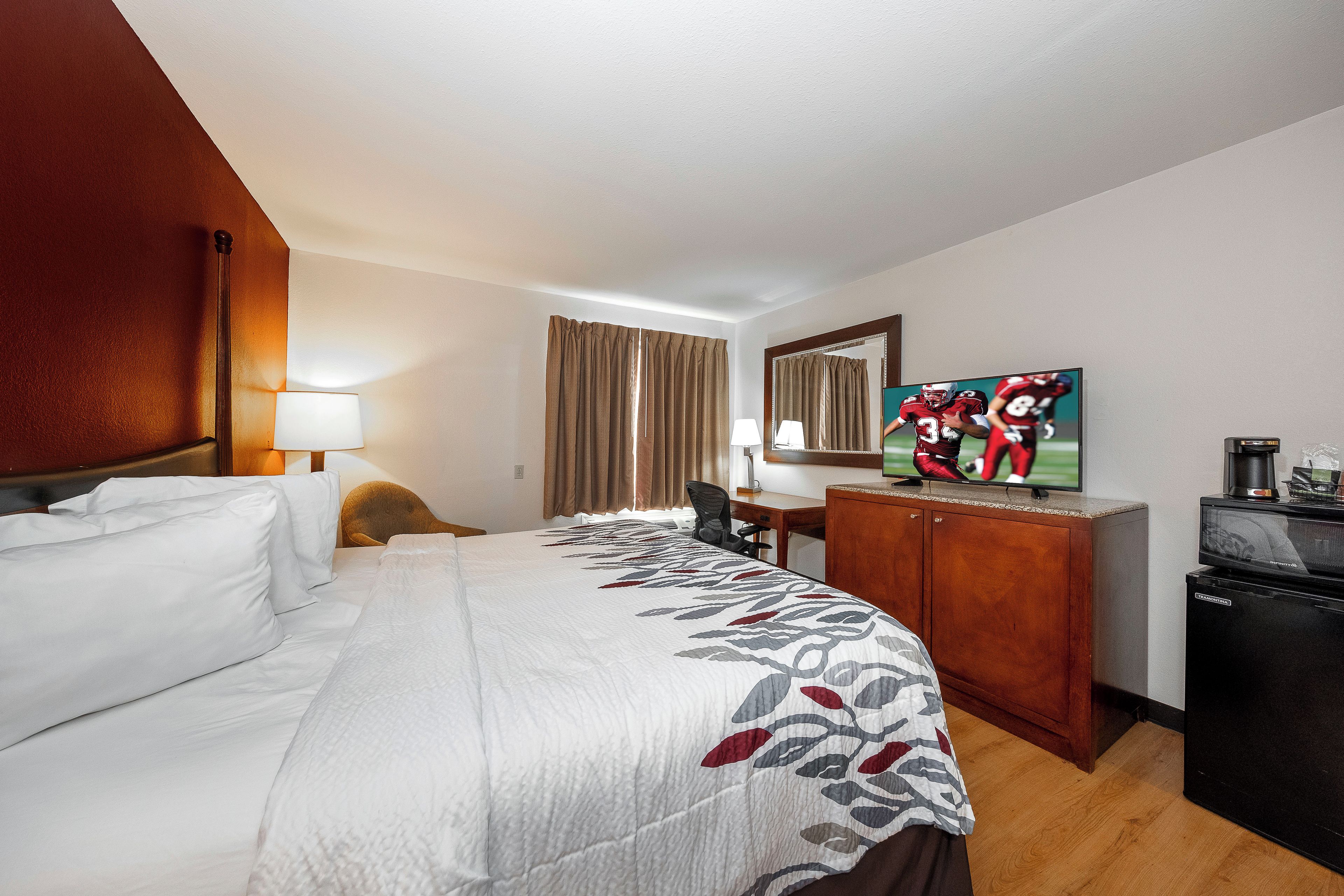A hotel room with a large bed, a desk, a television, and a wardrobe.
