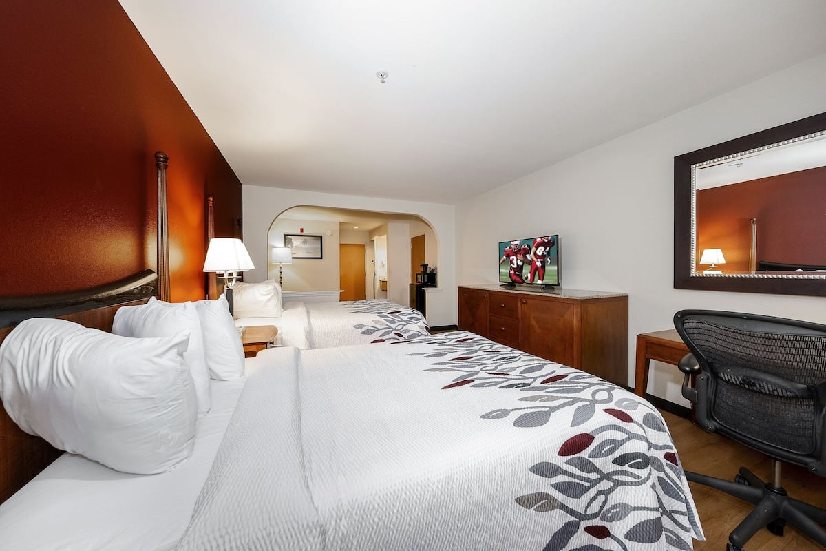 A hotel room with a large bed, a desk, a chair, a lamp, a painting, and a mirror.