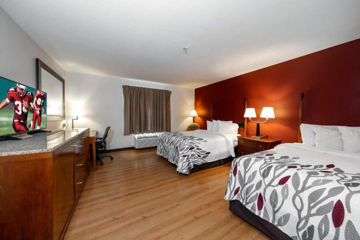 A hotel room with two beds, a desk, a television, and a window with curtains.