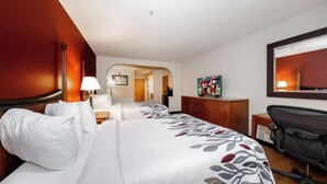 Quarto de hotel com cama, mesa de cabeceira, abajur, escrivaninha, cadeira e televisão.