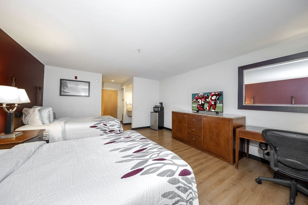 A hotel room with two beds, a desk, a chair, a TV, and a large mirror.