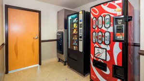Corredor com máquinas de venda automática, uma porta e piso cerâmico.