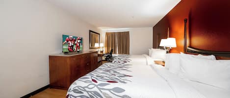Habitación de hotel con una cama grande, un escritorio con computadora, una silla, una lámpara y un cuadro en la pared.