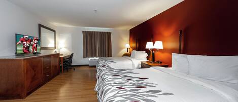 A hotel room with a bed, a desk, a chair, a TV, and a window with curtains.