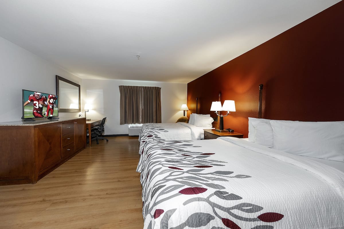 Ein Hotelzimmer mit einem großen Bett, einem Schreibtisch, einem Sessel, einem Fernseher und einem Fenster mit Vorhängen.