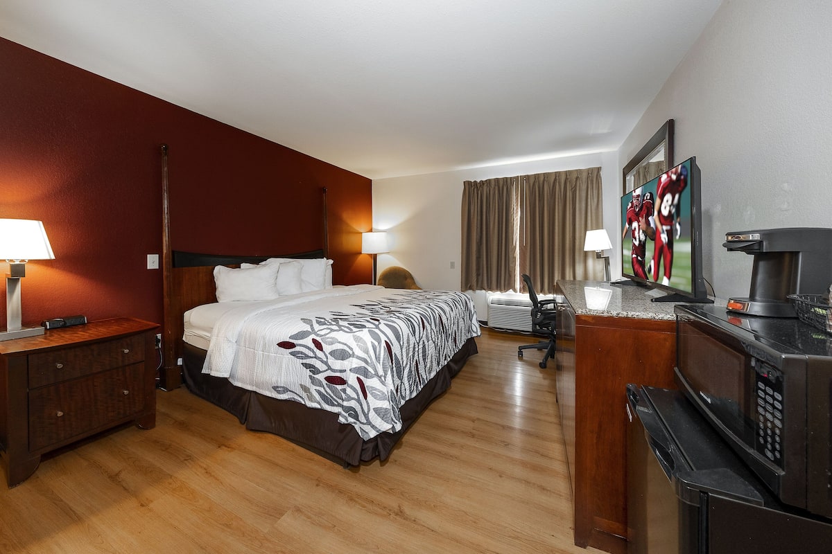 Ein Hotelzimmer mit Bett, Nachttisch, Lampe, Fernseher und einer Küchenzeile.