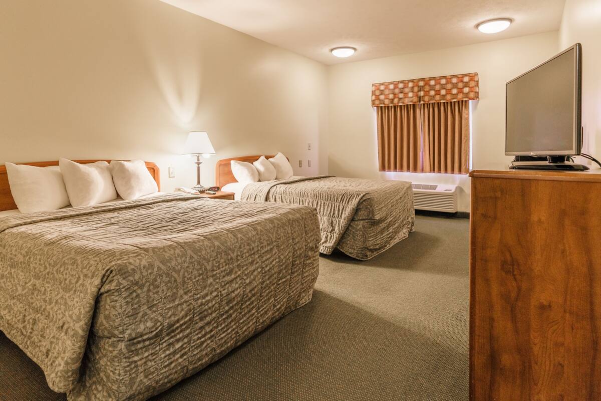 A hotel room with two beds, a TV, a lamp, and a window with curtains.