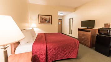 A hotel room with a bed, a desk, a lamp, a television, a microwave, and a dresser.