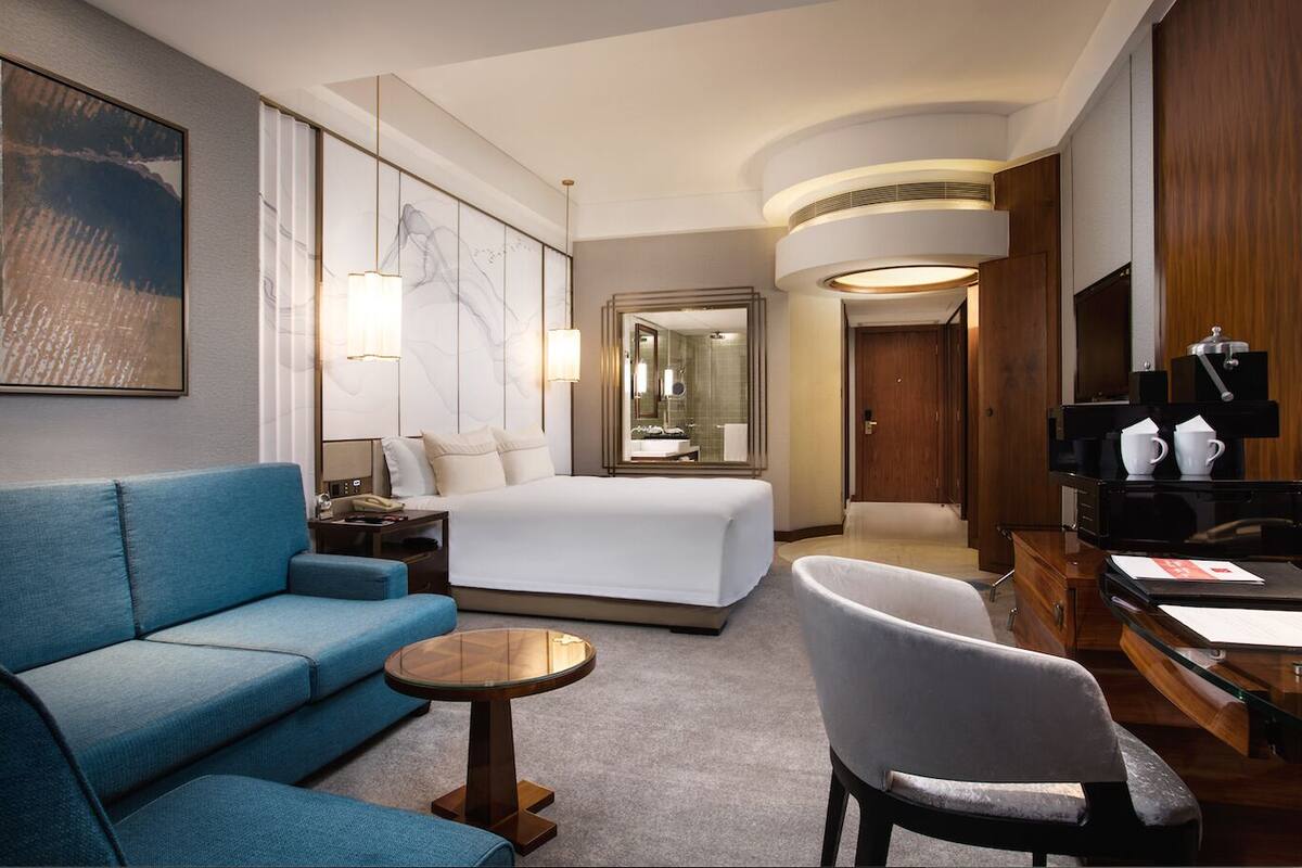 Ein Hotelzimmer mit einem großen Bett, einem blauen Sofa, einem runden Couchtisch und einem Schreibtisch mit Kaffeemaschine.