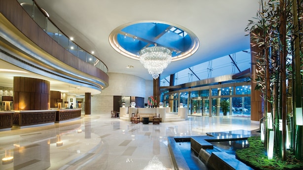 Un hall d’entrée spacieux avec un plafond haut, un lustre central et un comptoir de réception.