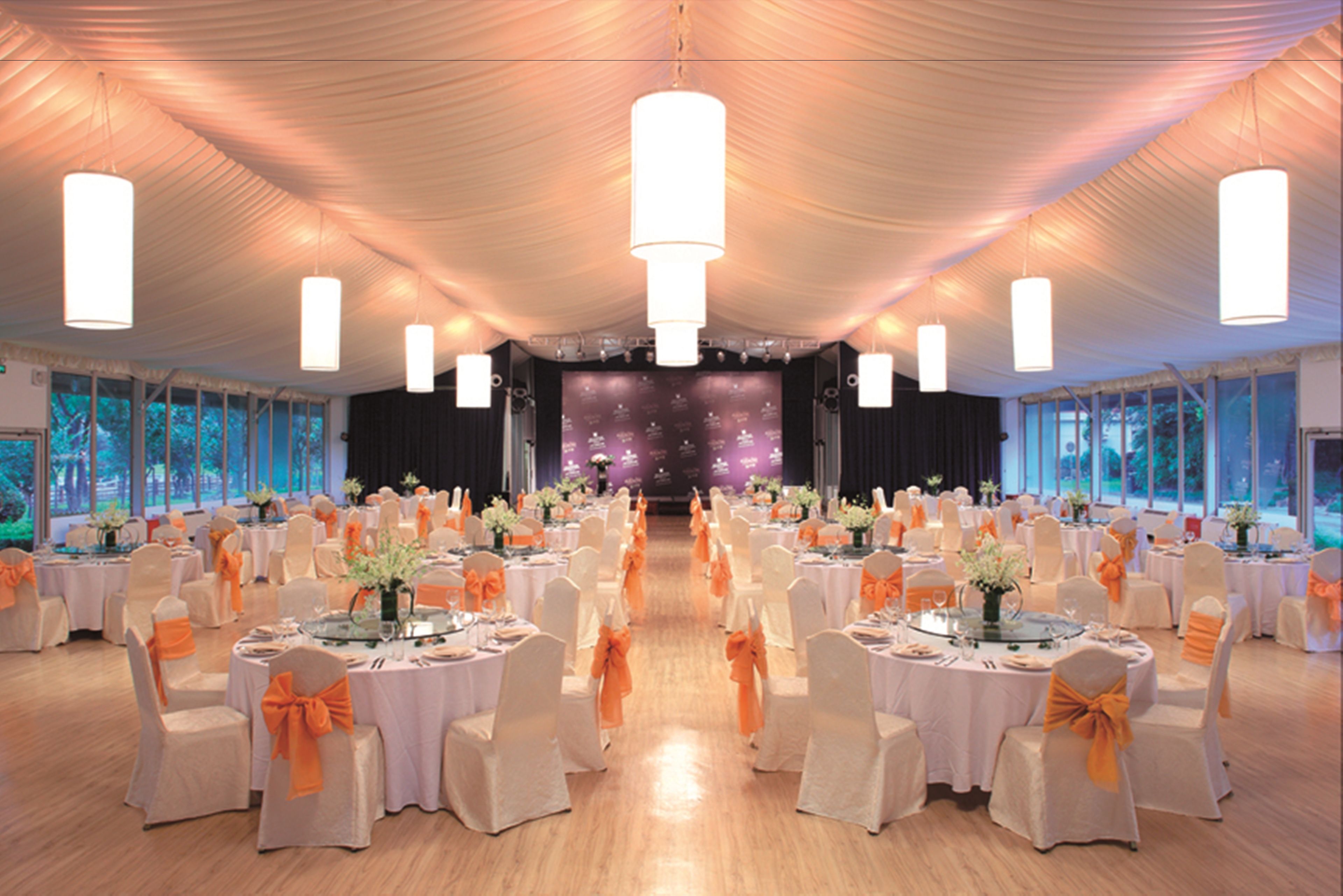 Une salle de banquet avec des tables rondes, des nappes blanches et des rubans orange.