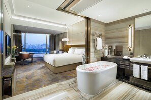 Een moderne hotelkamer met een groot bed, een badkuip met rozenblaadjes, een bureau en uitzicht op de stad.
