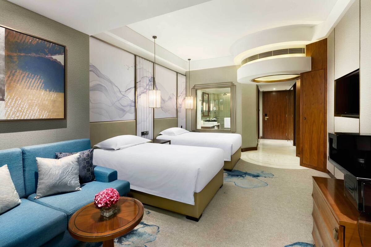 Ein Hotelzimmer mit einem Bett, einer Couch, einem Fernseher und einem durch eine Glastür einsehbaren Badezimmer.