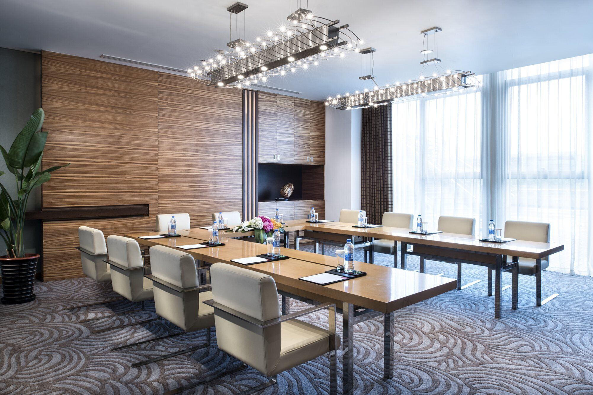 A conference room with a long table, chairs, a potted plant, and a decorative light fixture.