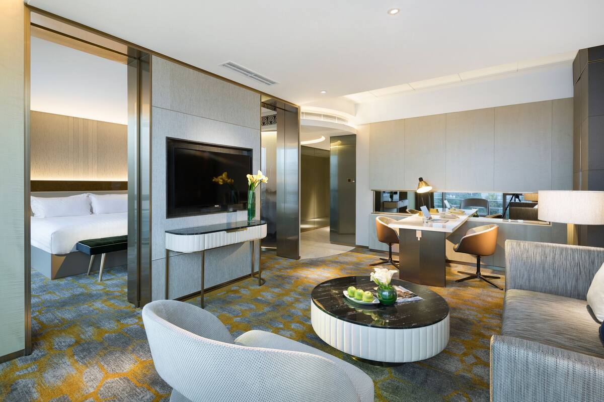 Ein modernes Hotelzimmer mit Bett, Fernseher, Essbereich und Sitzecke mit Couchtisch.
