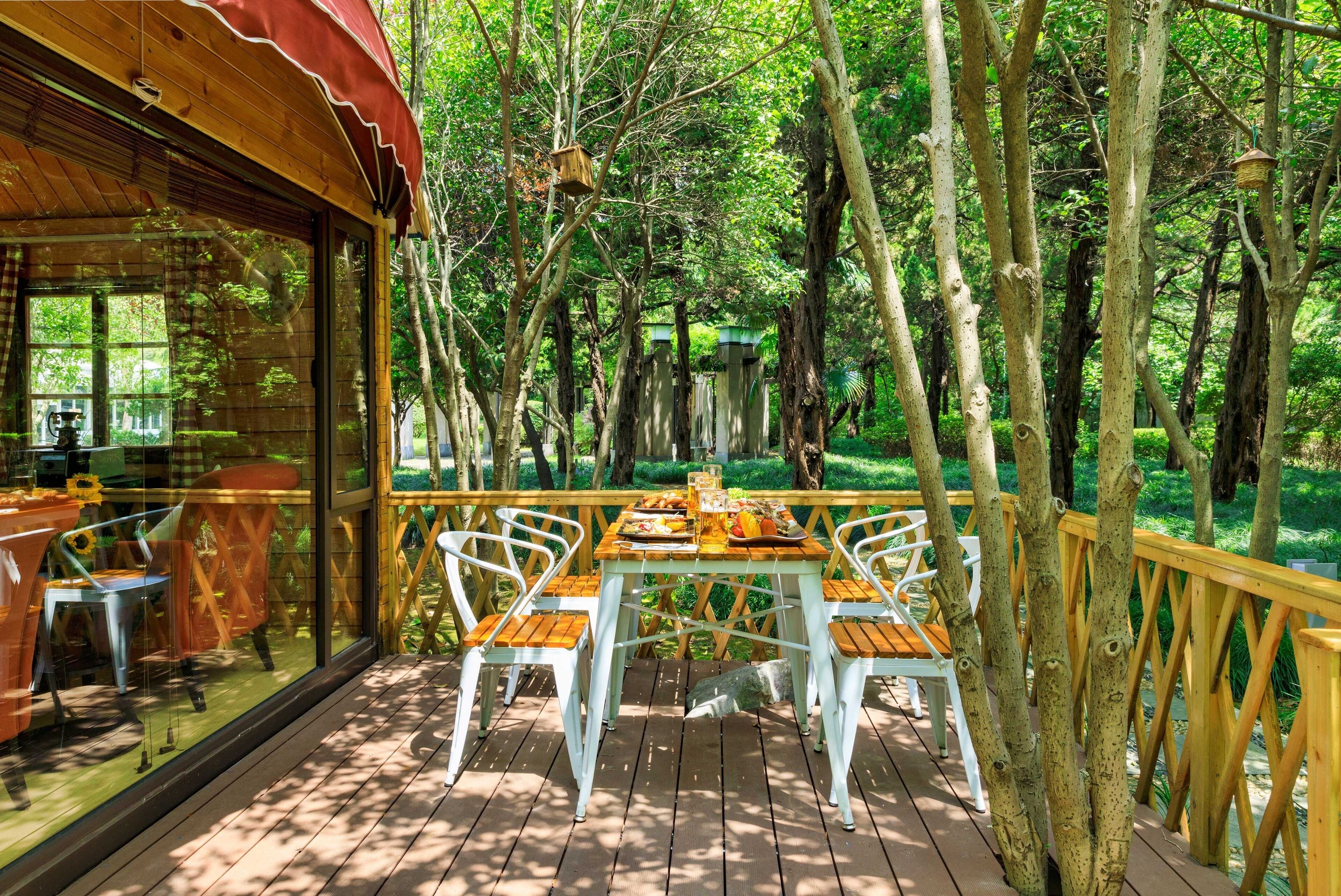 A wooden deck with a table and chairs, surrounded by trees.