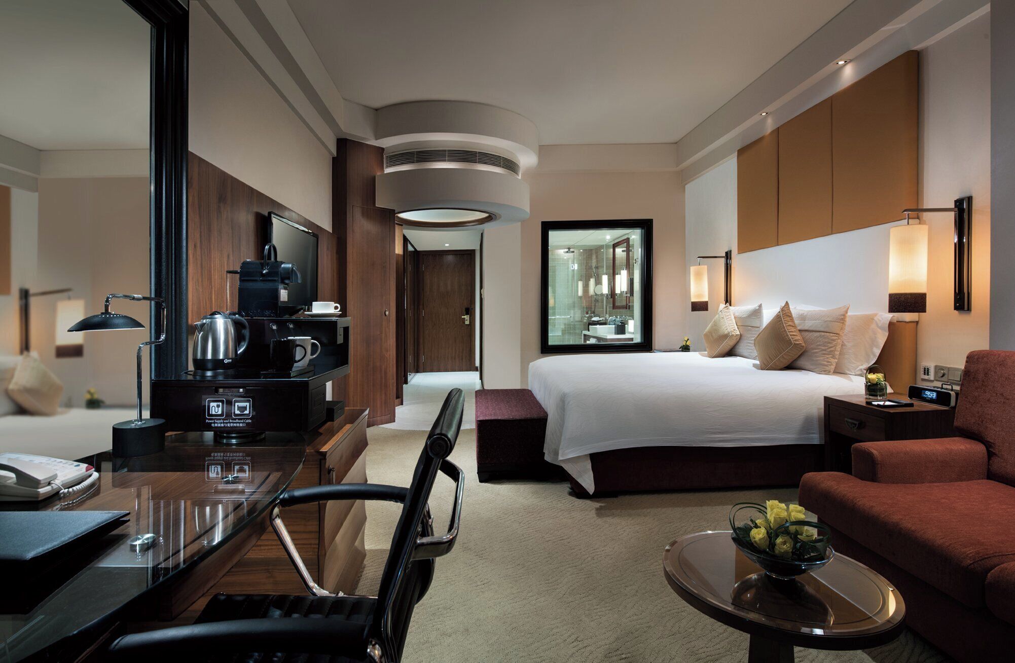 Ein Hotelzimmer mit Bett, Schreibtisch mit Kaffeemaschine, Fernseher und einer Sitzecke mit Sofa und Sessel.