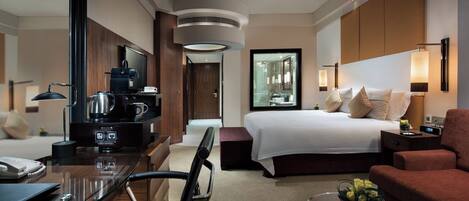 Ein Hotelzimmer mit Bett, Schreibtisch mit Kaffeemaschine, Fernseher und einer Sitzecke mit Sofa und Sessel.