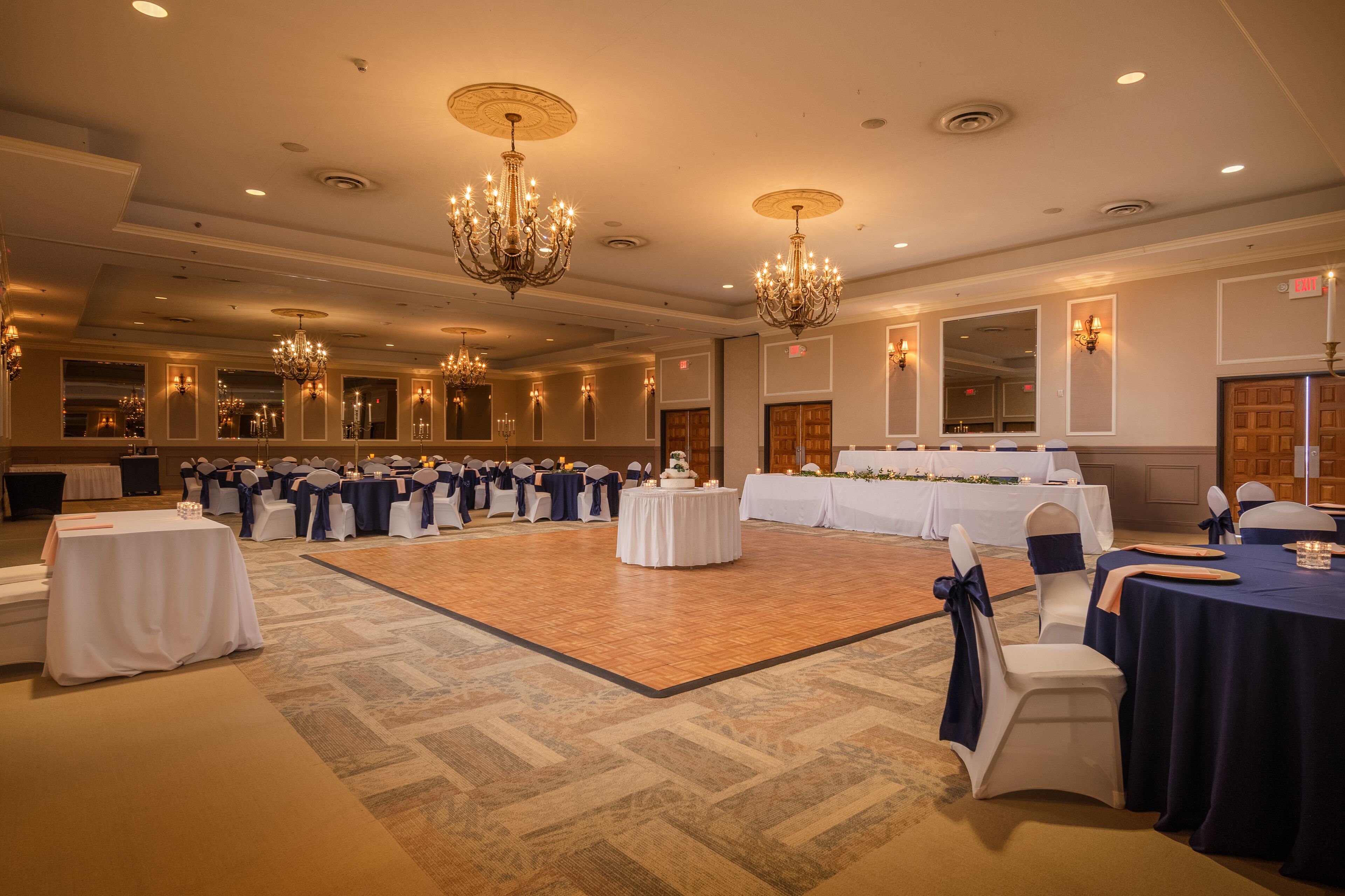 Un gran salón de baile con mesas redondas, sillas, candelabros y una pista de baile.