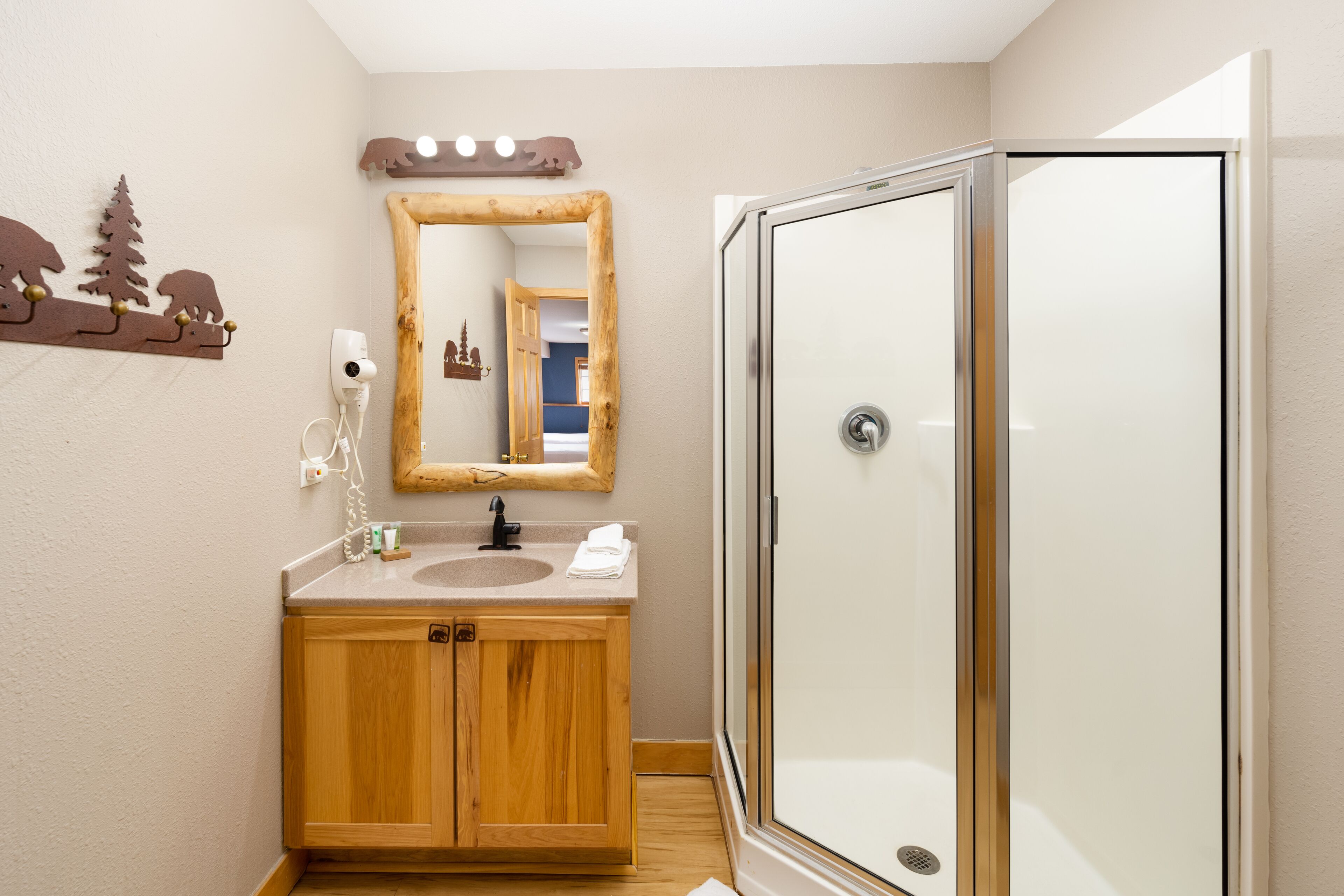 A bathroom with a wooden vanity, a mirror, a shower enclosure, and a wall-mounted towel rack.