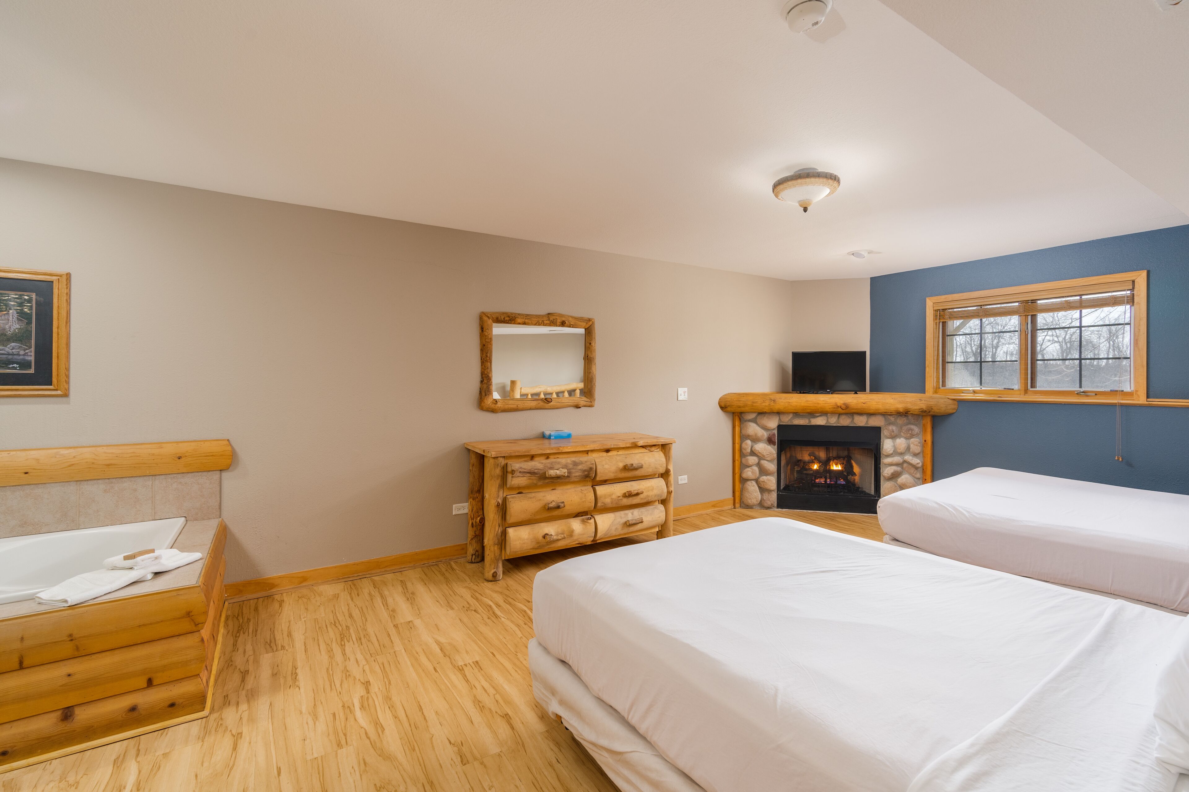 A bedroom with two beds, a wooden dresser, a fireplace, and a television.