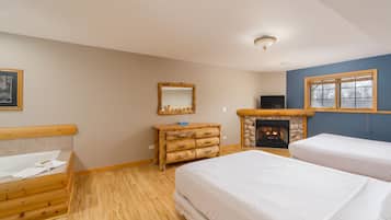 A bedroom with two beds, a wooden dresser, a fireplace, and a television.