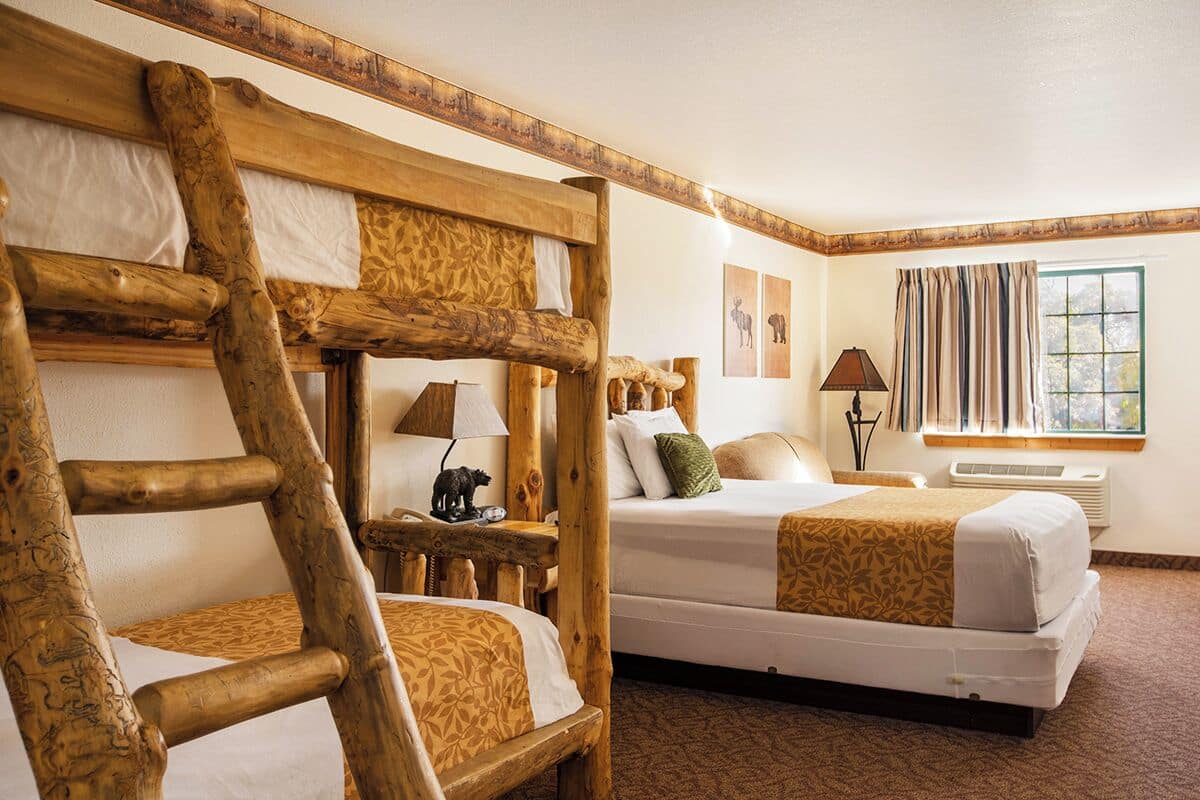 Une chambre avec deux lits, des têtes de lit en bois, une lampe, une fenêtre avec des rideaux et un climatiseur fixé au mur.