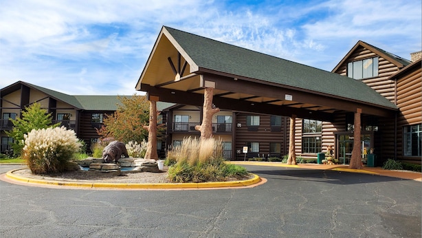 A log cabin-style building with a covered entrance, a landscaped area with rocks and shrubs, and a clear sky.