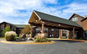 A log cabin-style building with a covered entrance, a landscaped area with rocks and shrubs, and a clear sky. - Grand Bear Resort at Starved Rock (Utica)