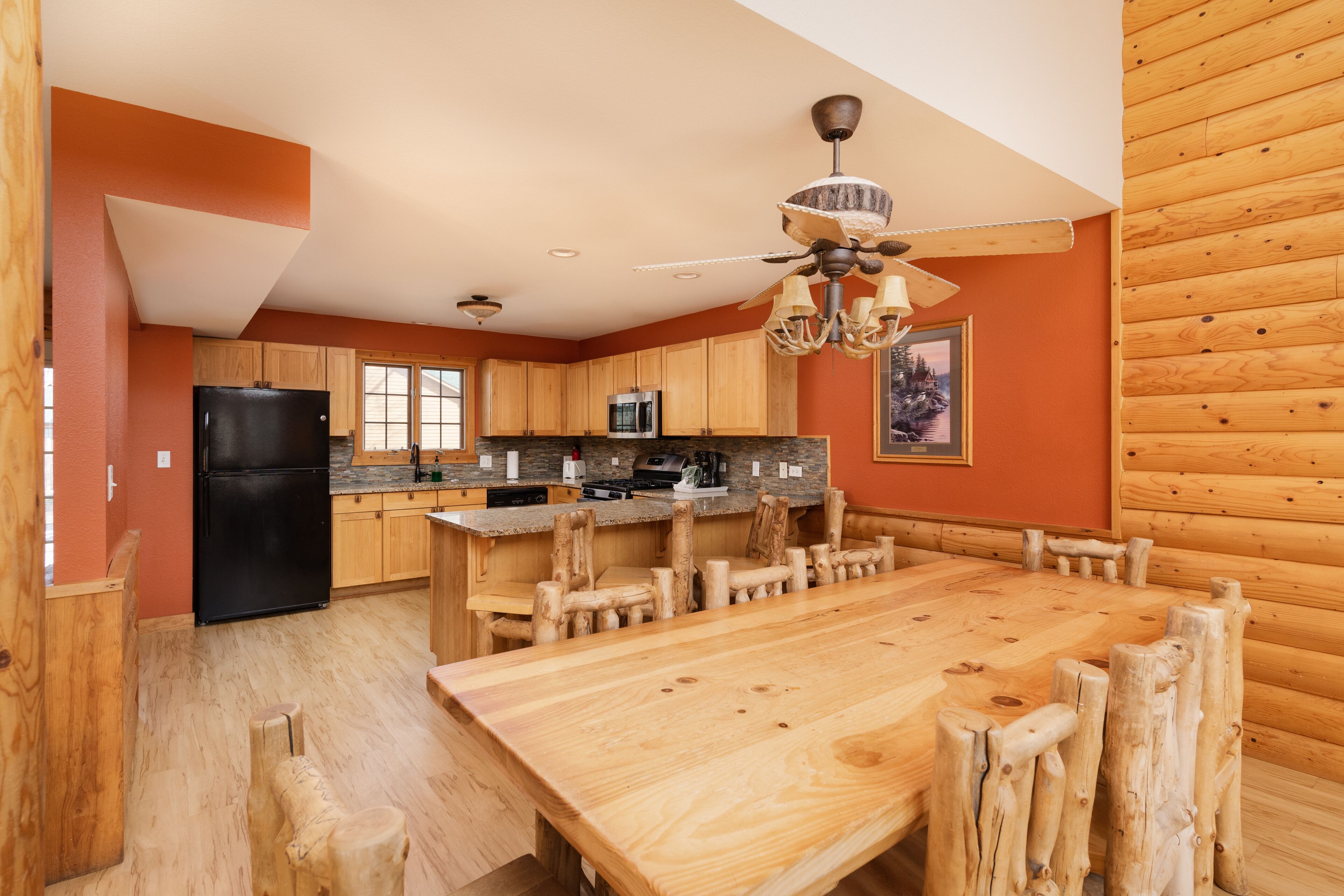 A spacious kitchen with wooden cabinets, a black refrigerator, a wooden dining table, and a ceiling fan.