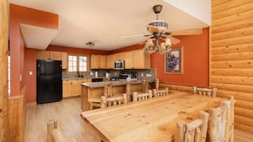 A spacious kitchen with wooden cabinets, a black refrigerator, a wooden dining table, and a ceiling fan.
