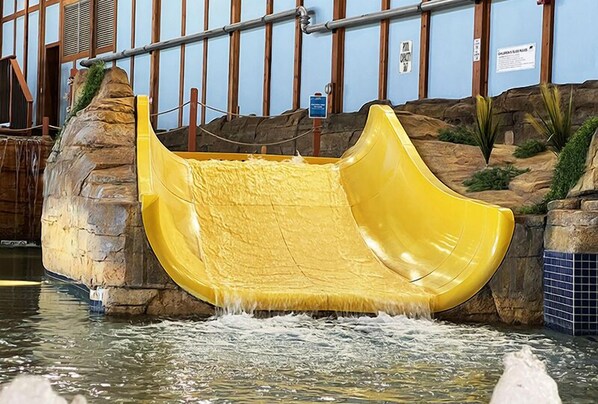 A yellow water slide in a pool area with a rocky backdrop and a blue tiled wall.
