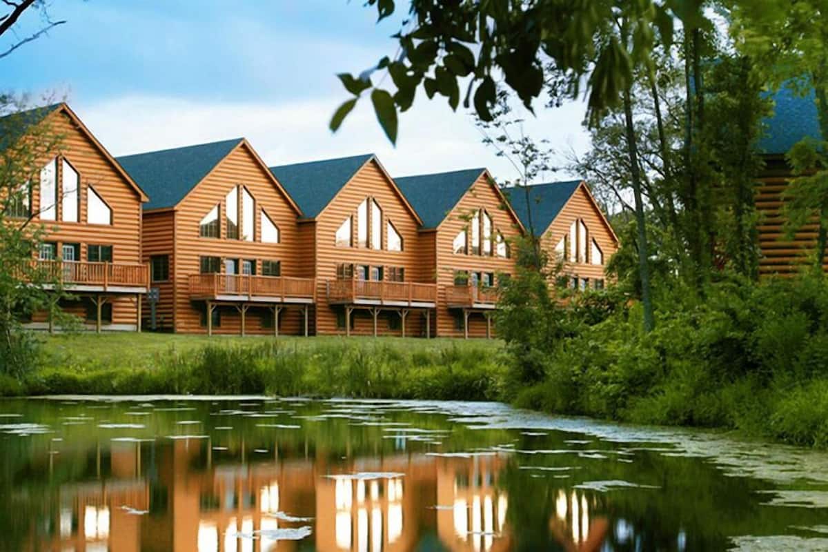 Une rangée de chalets en bois, dotés de grandes fenêtres et de balcons, situés au bord d’un lac paisible.